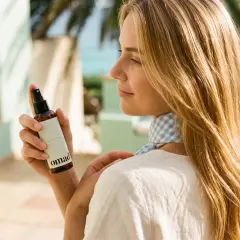 Kobieta z długimi, blond włosami używa sprayu do pielęgnacji długich włosów.