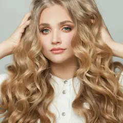 Blondynka z burzą falujących włosów, które przypominają loki na pasek od szlafroka, w białej koszuli.