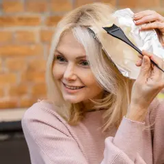 Kobieta z blond włosami wykonuje podział włosów na sekcje do farbowania, używając folii i pędzelka.