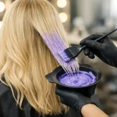 Fryzjer nakłada fioletową farbę na rozjaśnione blond włosy. Szukasz idealnej farby na rude włosy po rozjaśnianiu?