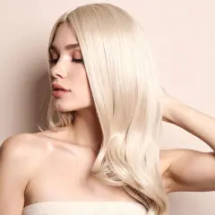 Kobieta z burzą platynowy blond włosów, delikatnie dotyka swojej szyi.