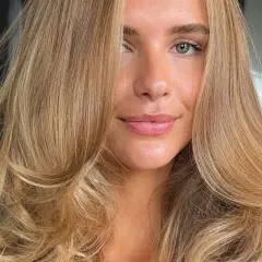 Kobieta z pięknymi, falowanymi włosami w odcieniu ciepły blond. Jej spojrzenie jest delikatne, a usta lekko rozchylone.