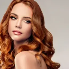Miedziany blond dla kogo? Dla kobiety z falowanymi włosami i subtelnym makijażem, która emanuje elegancją i pewnością siebie.