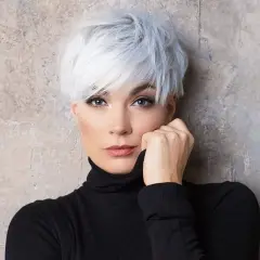 Kobieta z siwymi włosami w stylu pixie bob fryzura, ubrana w czarny golf, opiera dłoń o twarz.