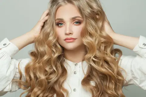 Blondynka z burzą falujących włosów, które przypominają loki na pasek od szlafroka, w białej koszuli.
