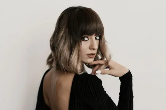 Kobieta z ciemnymi, ombre włosami w stylu blunt bob, zmysłowo spogląda przez ramię.