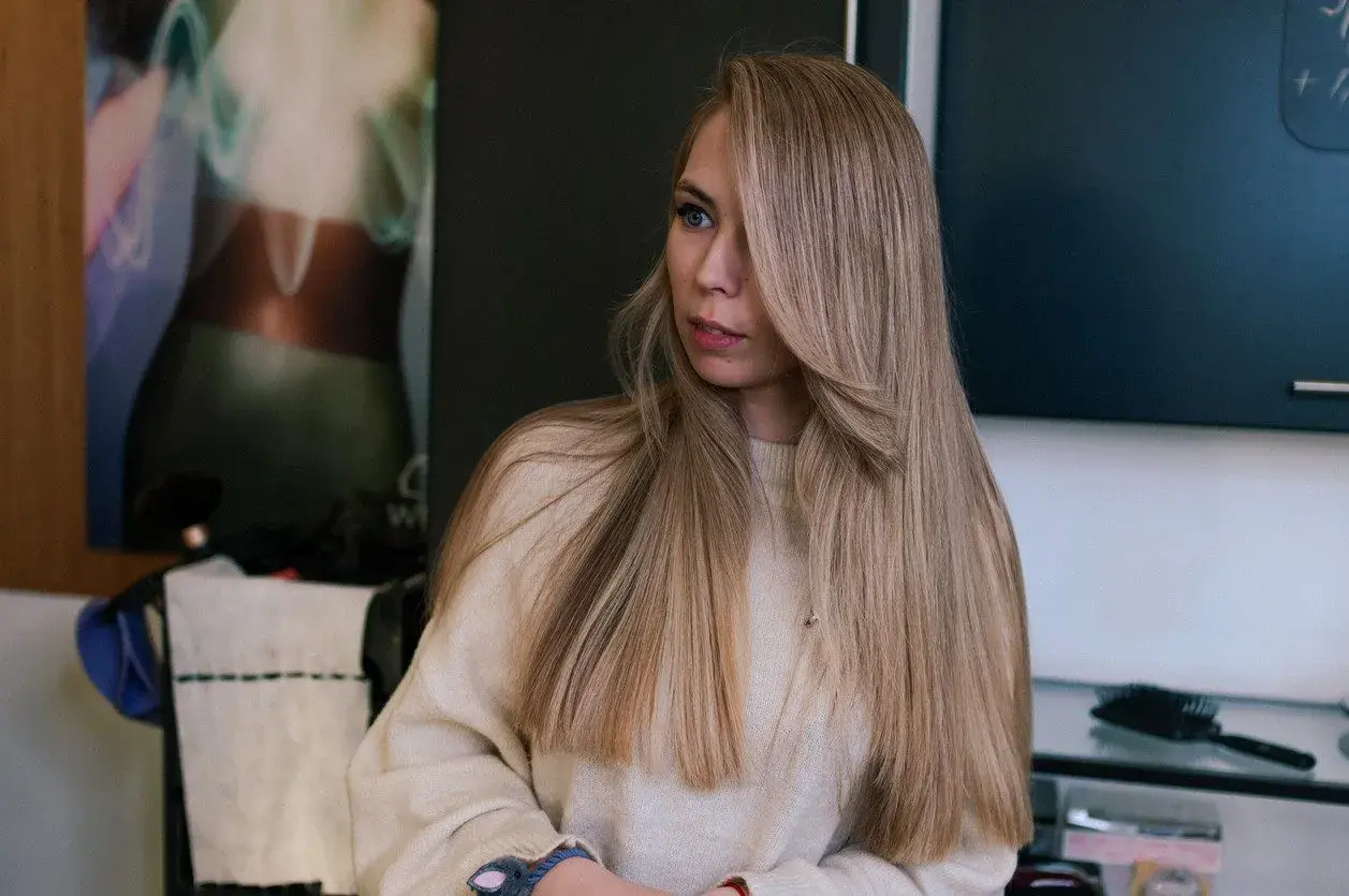 Dziewczyna z długimi, mysi blond włosami, ubrana w beżowy sweter.