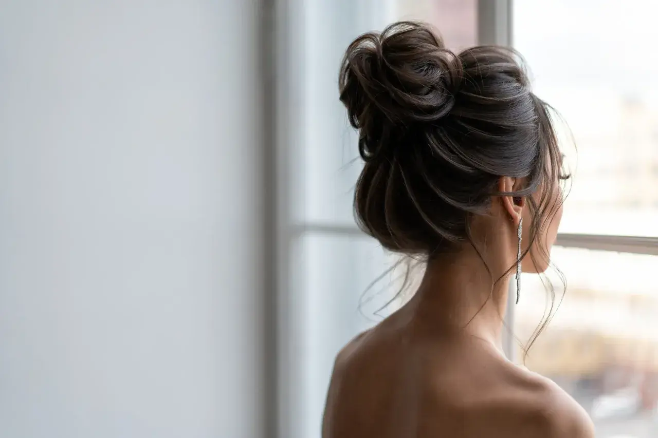 Elegancki messy bun jak zrobić? Luźno upięte włosy, delikatne pasma opadające na ramiona, długie kolczyki.
