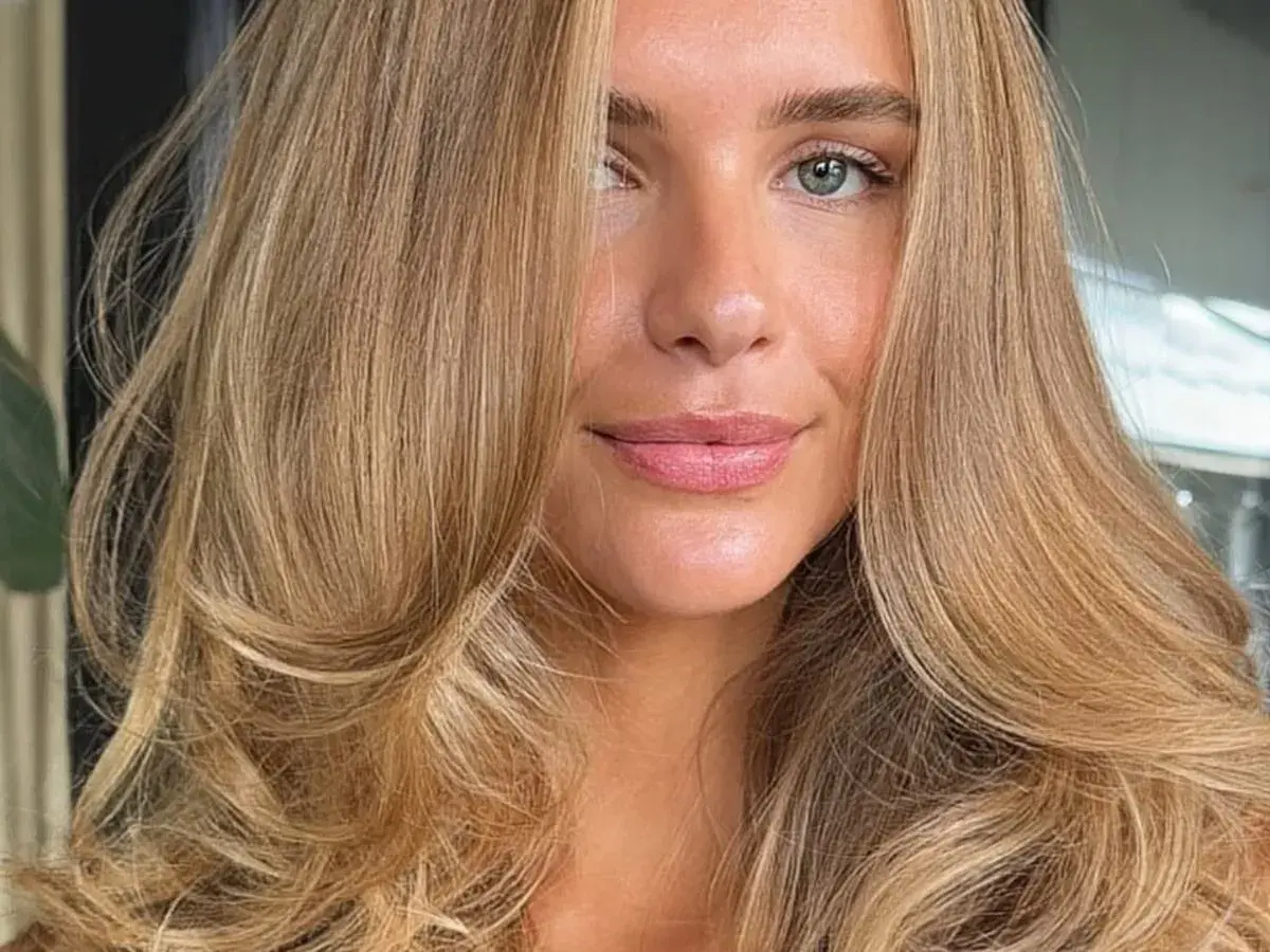 Kobieta z pięknymi, falowanymi włosami w odcieniu ciepły blond. Jej spojrzenie jest delikatne, a usta lekko rozchylone.
