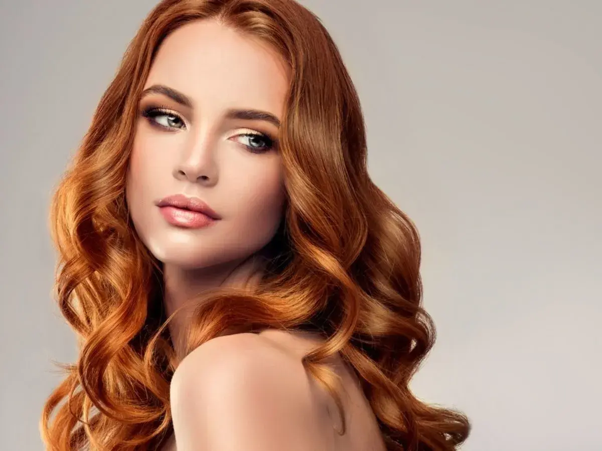 Miedziany blond dla kogo? Dla kobiety z falowanymi włosami i subtelnym makijażem, która emanuje elegancją i pewnością siebie.
