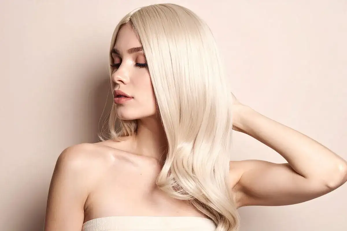 Kobieta z burzą platynowy blond włosów, delikatnie dotyka swojej szyi.